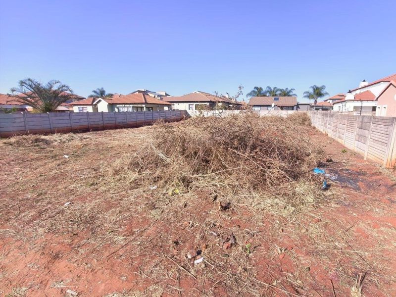 A vacant residential plot enclosed by precast concrete boundary walls, currently featuring overgrown vegetation and accumulated debris.