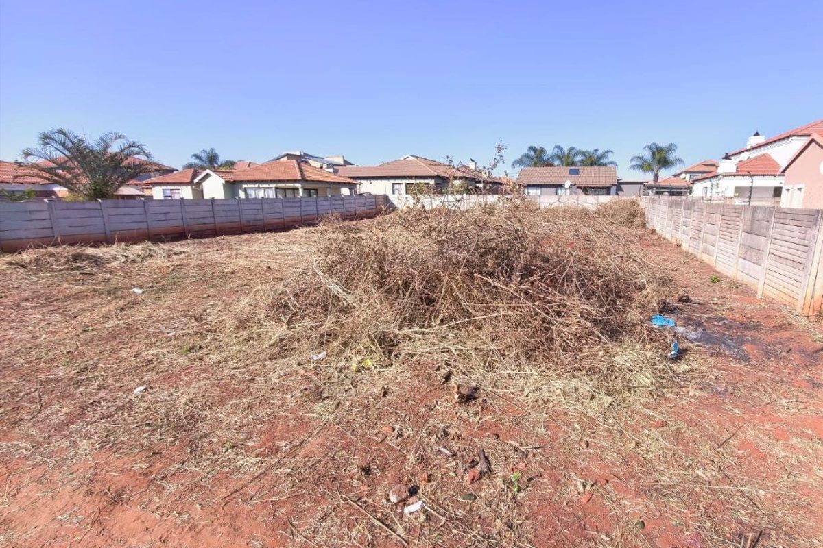 A vacant residential plot enclosed by precast concrete boundary walls, currently featuring overgrown vegetation and accumulated debris.