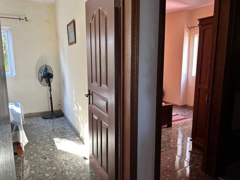 A hallway area featuring tiled flooring and timber doors, showing signs of wear on the walls requiring maintenance and cosmetic updates.