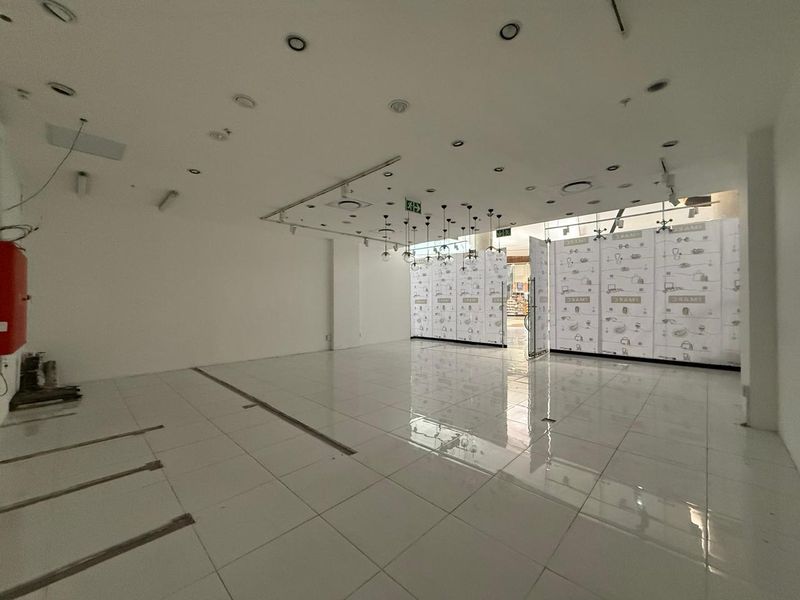 An empty retail space featuring white tiled flooring, recessed ceiling lighting, and a glass storefront, suitable for a variety of commercial business applications.