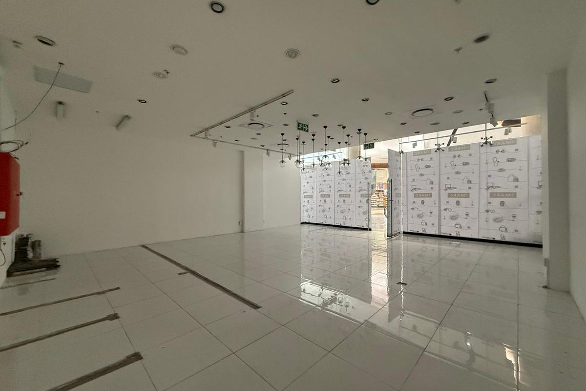 An empty retail space featuring white tiled flooring, recessed ceiling lighting, and a glass storefront, suitable for a variety of commercial business applications.