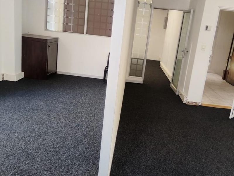 An open-plan office space featuring dark carpeting, partition walls, and exposed industrial ducting, offering a functional layout for a professional work environment.