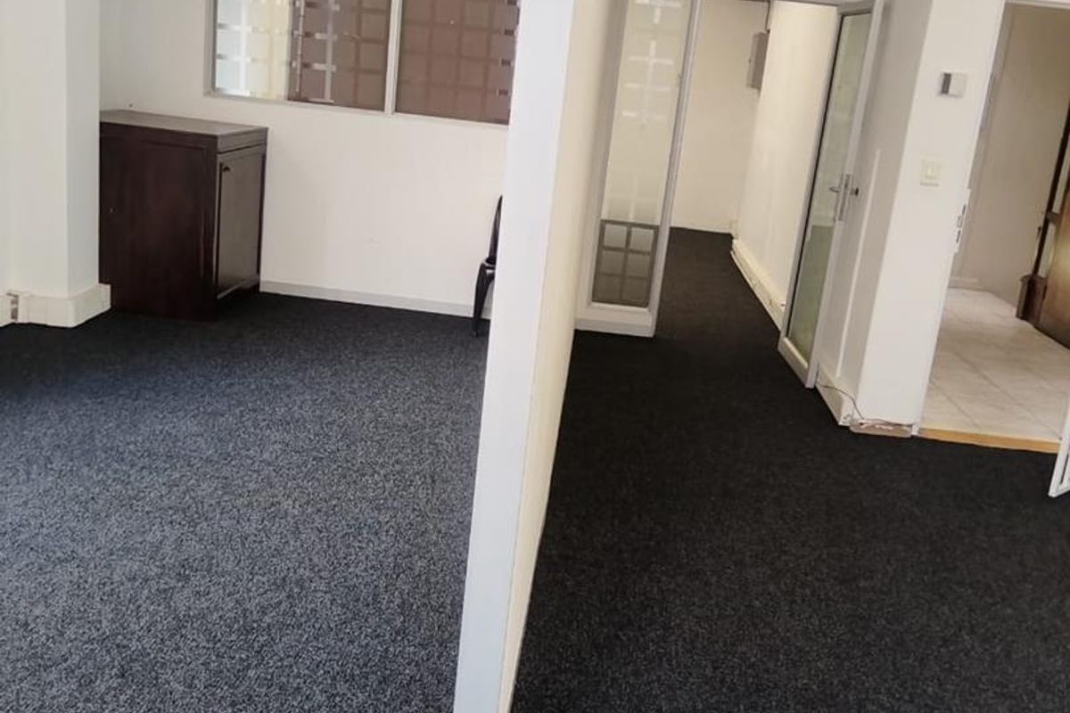 An open-plan office space featuring dark carpeting, partition walls, and exposed industrial ducting, offering a functional layout for a professional work environment.