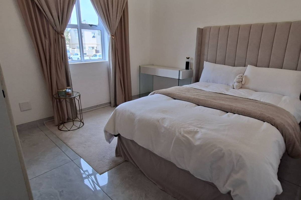 A well-maintained bedroom featuring neutral tones, large format floor tiles, and a window providing natural light.