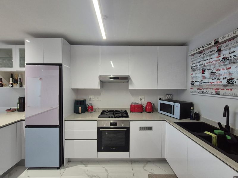 Modern kitchen featuring white high-gloss cabinetry, stone countertops, integrated gas hob, electric oven, and sleek tiled flooring.