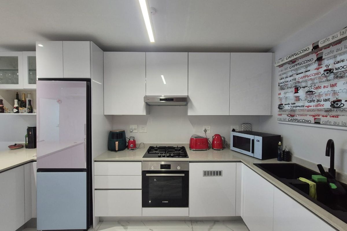 Modern kitchen featuring white high-gloss cabinetry, stone countertops, integrated gas hob, electric oven, and sleek tiled flooring.