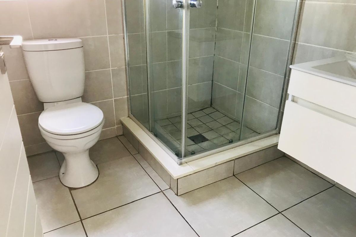 A functional bathroom featuring a glass-enclosed shower, a white ceramic toilet, and a wall-mounted vanity unit with a basin.