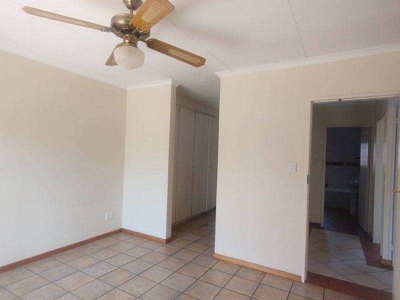 An empty bedroom featuring tiled flooring, a ceiling fan, and built-in cupboards, with an adjacent en-suite bathroom visible through the doorway.