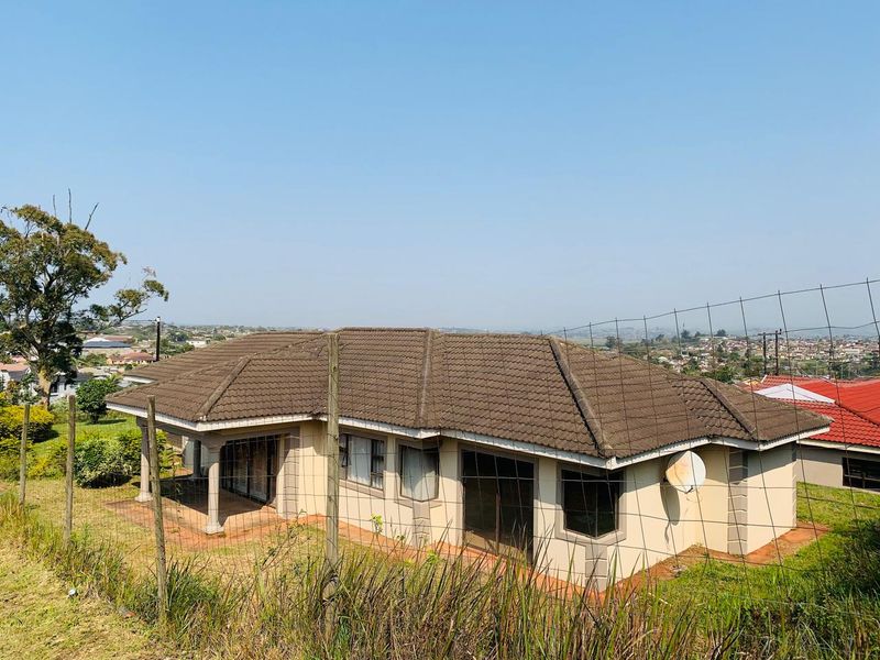Rear view of a single-story residential house featuring a covered patio, sliding glass doors, and concrete roof tiles, set in a suburban landscape.