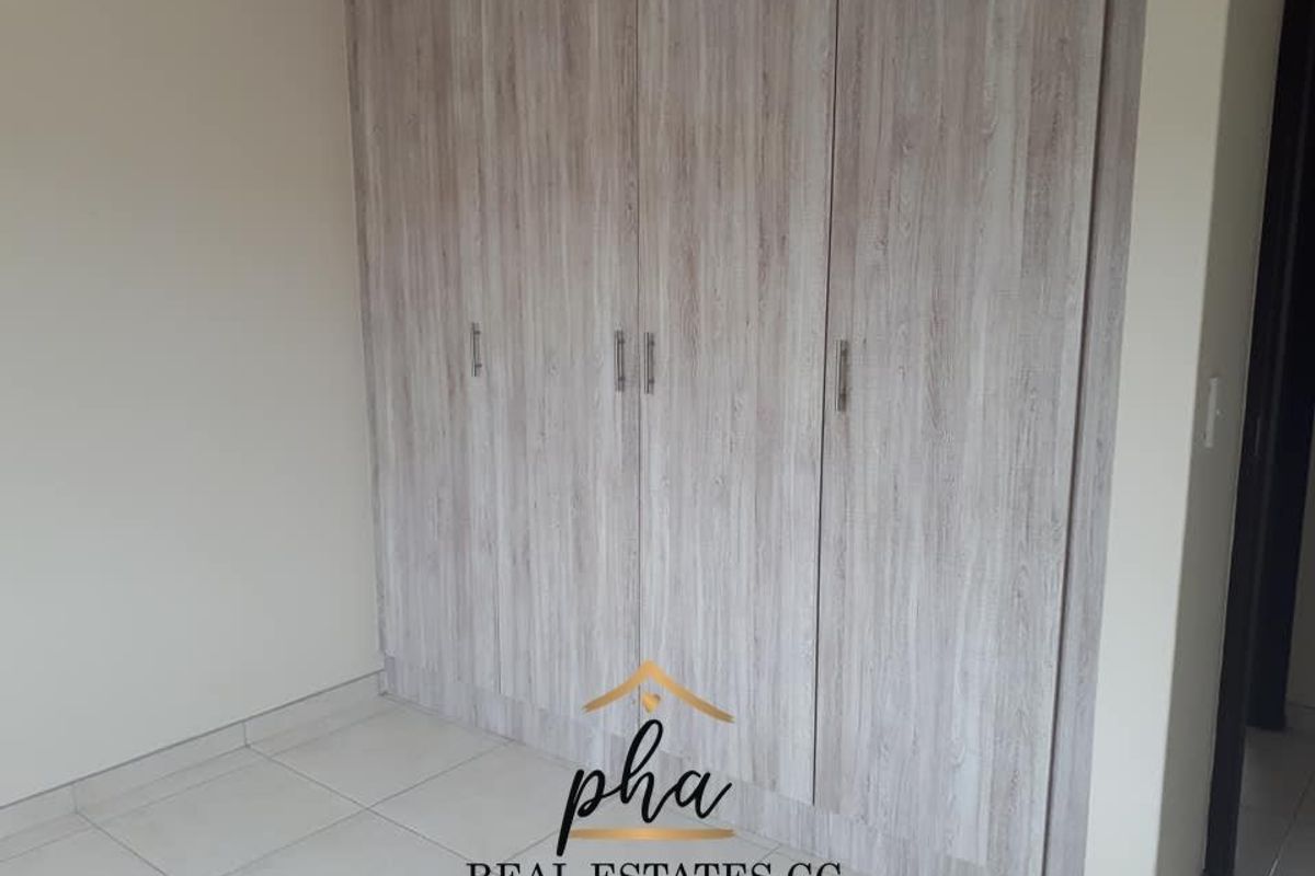 A bedroom featuring modern, light wood-grain built-in cupboards with sleek metal handles and neutral floor tiling.