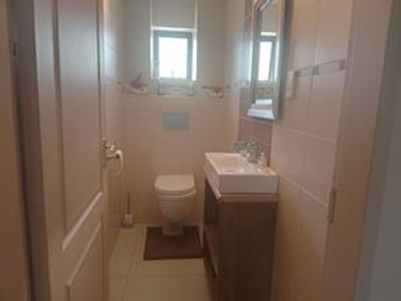 A compact bathroom featuring a wall-mounted toilet, vanity basin, and neutral wall tiling.