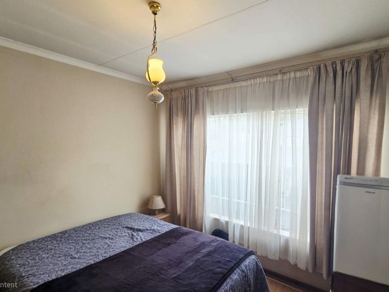 A standard bedroom featuring neutral walls, a central pendant light fixture, and window curtain tracks.