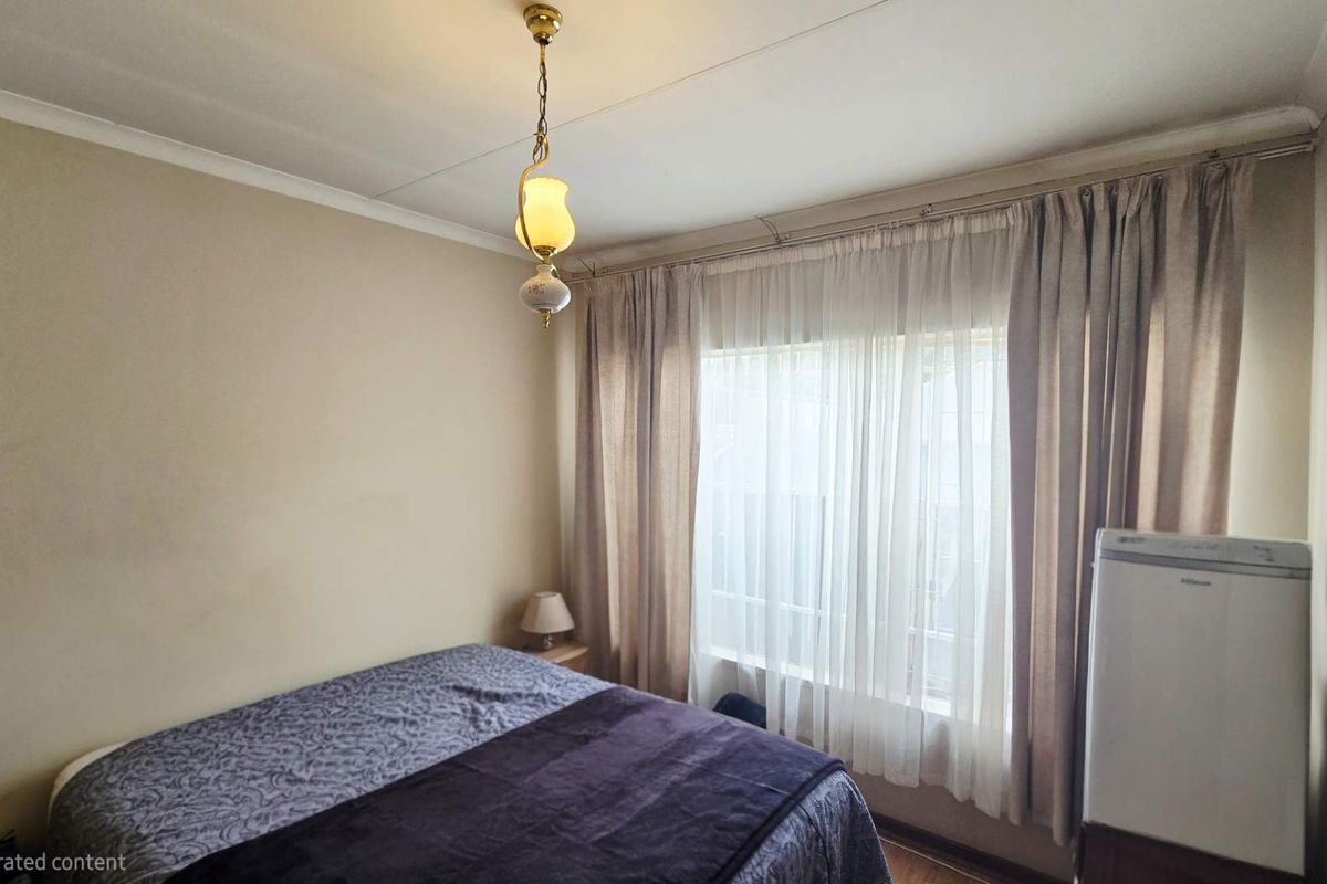A standard bedroom featuring neutral walls, a central pendant light fixture, and window curtain tracks.