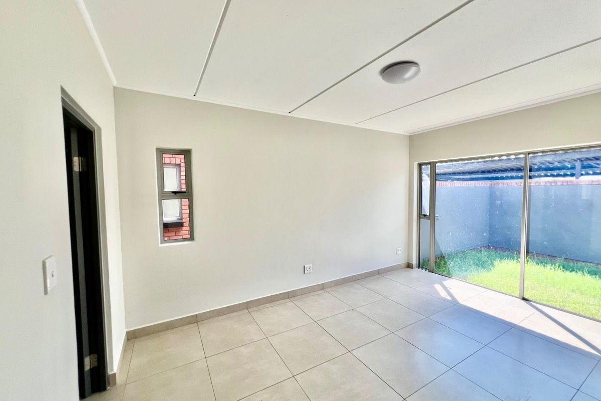 A bright, empty living room featuring neutral tiled flooring, large sliding glass doors leading to a private garden, and a modern ceiling finish.