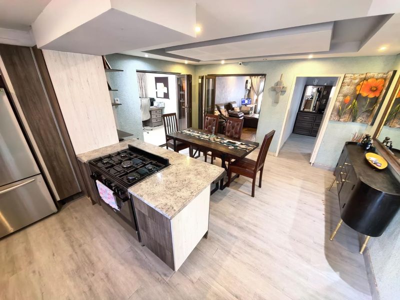 Open-plan kitchen and dining area featuring modern cabinetry, stone countertops, a gas stove, and recessed ceiling lighting with neutral laminate flooring throughout.