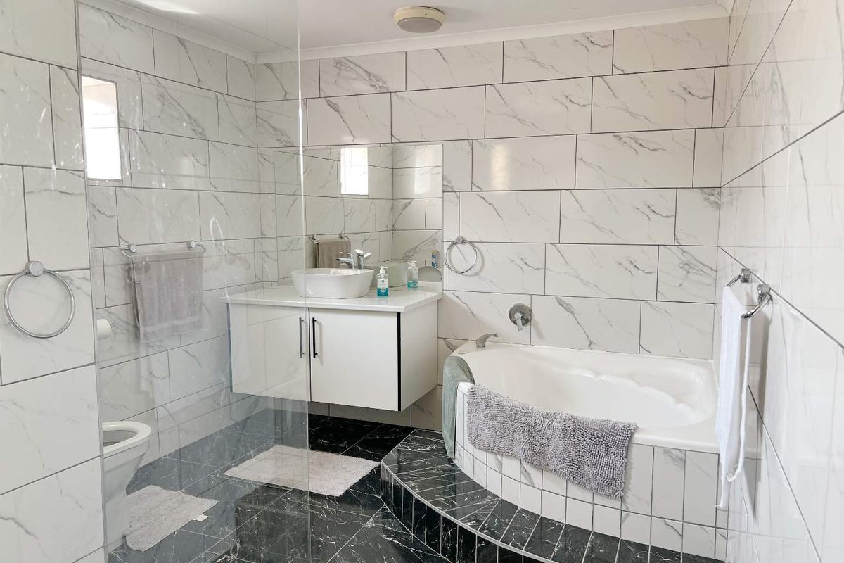 Modern bathroom featuring a corner bathtub, glass-enclosed shower, and a floating vanity with a vessel sink, finished with marble-look wall tiles and dark floor tiles.