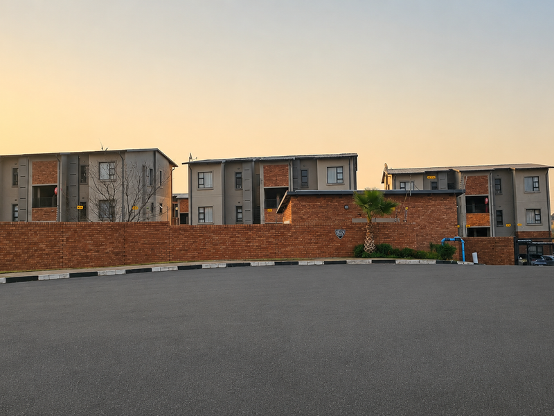 Exterior view of the Kilburn apartment complex featuring multi-story brick and plaster buildings, a secure perimeter wall, and paved driveway access.