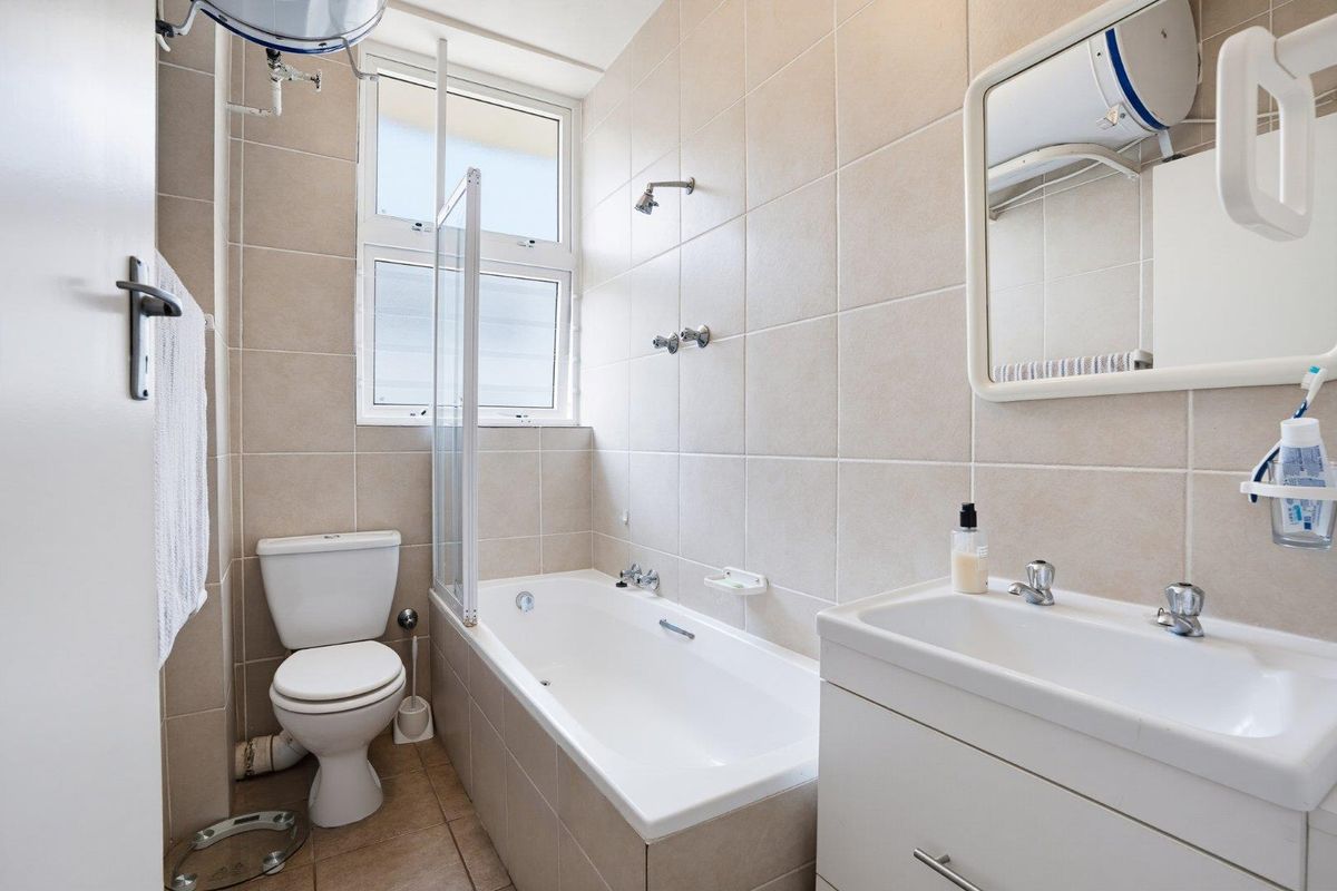 A functional bathroom featuring a bathtub with a shower screen, a vanity basin, and a toilet, finished with neutral wall and floor tiles.