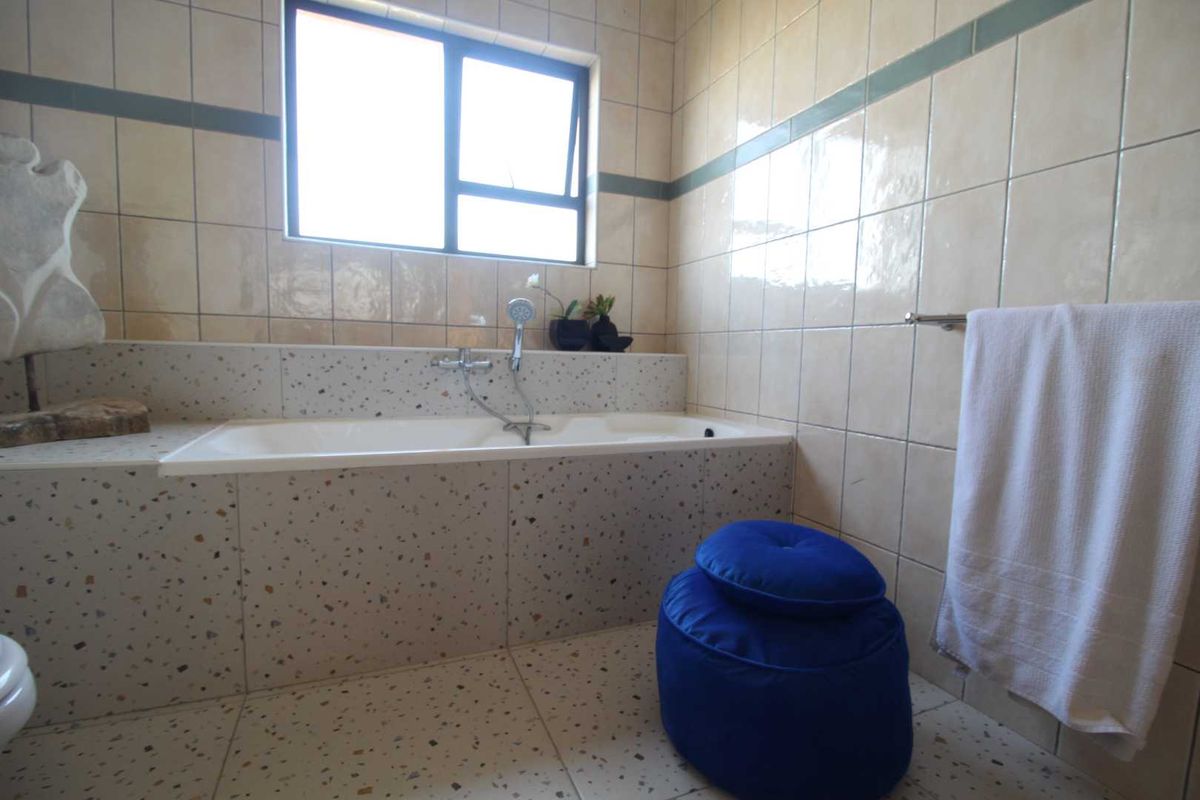 A bathroom featuring a built-in bathtub with a handheld shower mixer, finished with terrazzo-style tiling and neutral wall tiles.