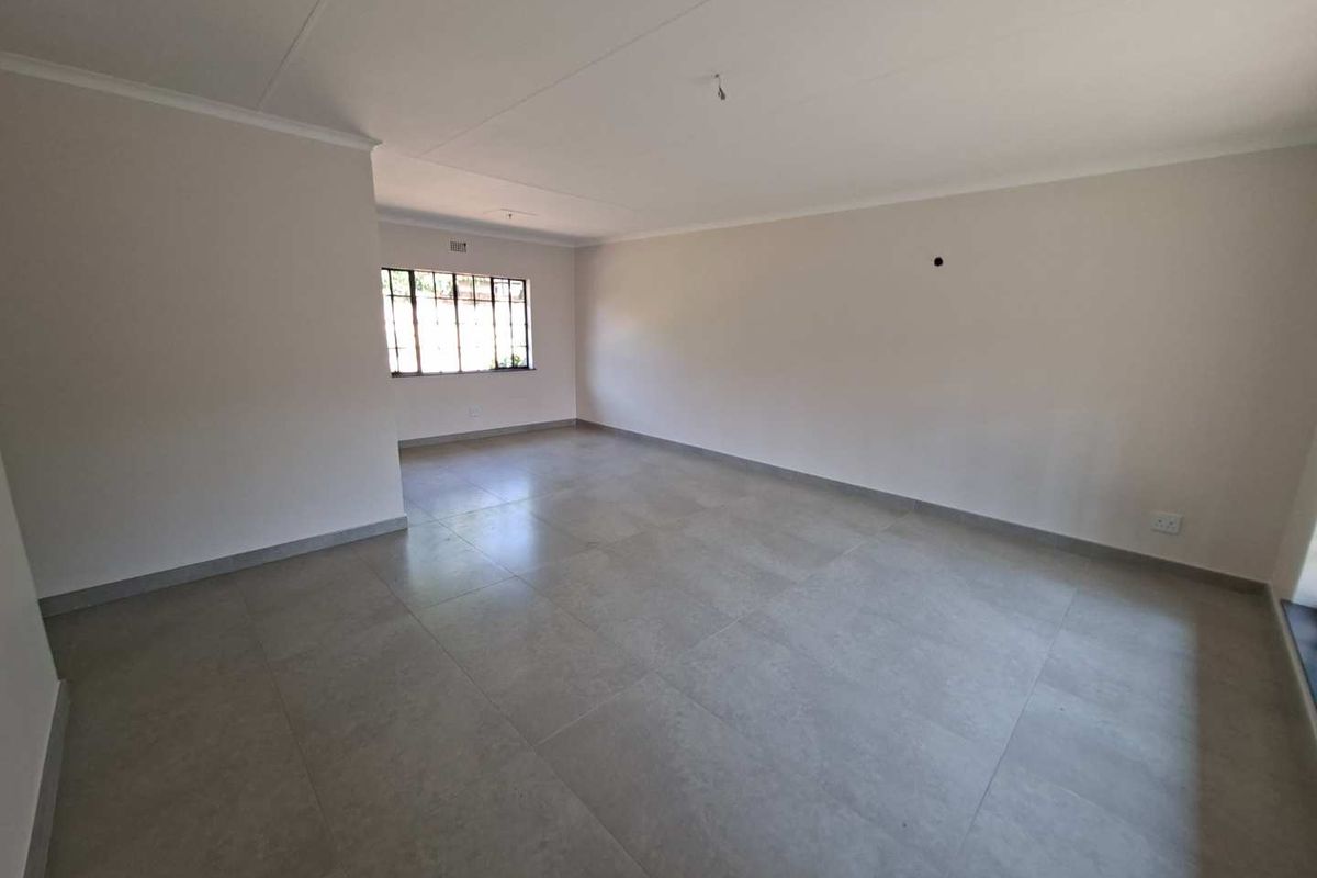 A spacious, empty living area featuring neutral tiled flooring, coved cornicing, and a steel-framed window, providing a clean canvas for interior design.