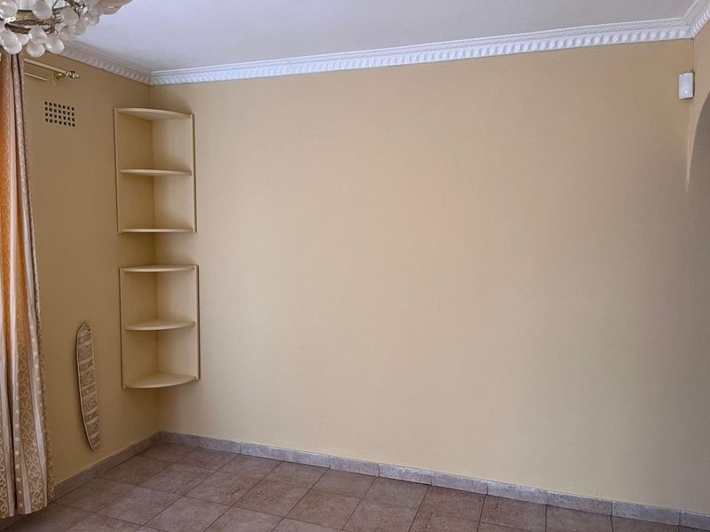 An empty living area featuring tiled flooring, decorative ceiling cornicing, and built-in corner shelving units.