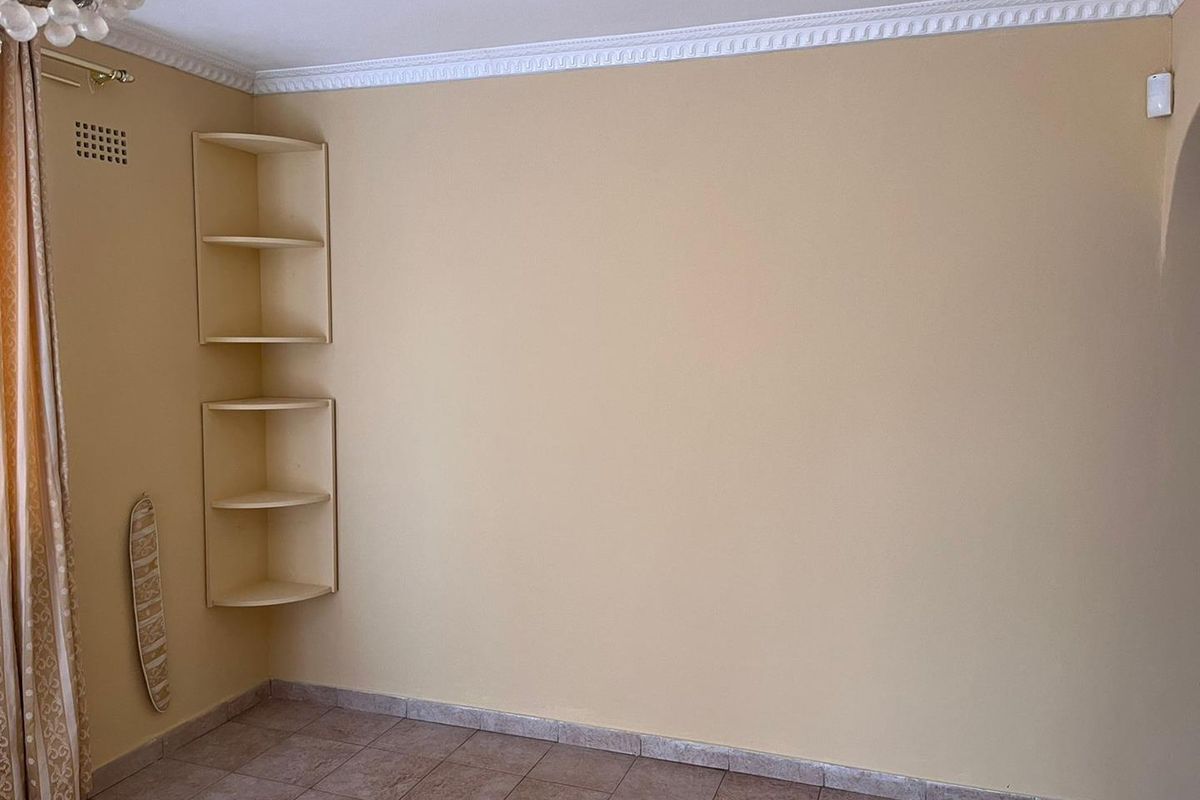 An empty living area featuring tiled flooring, decorative ceiling cornicing, and built-in corner shelving units.