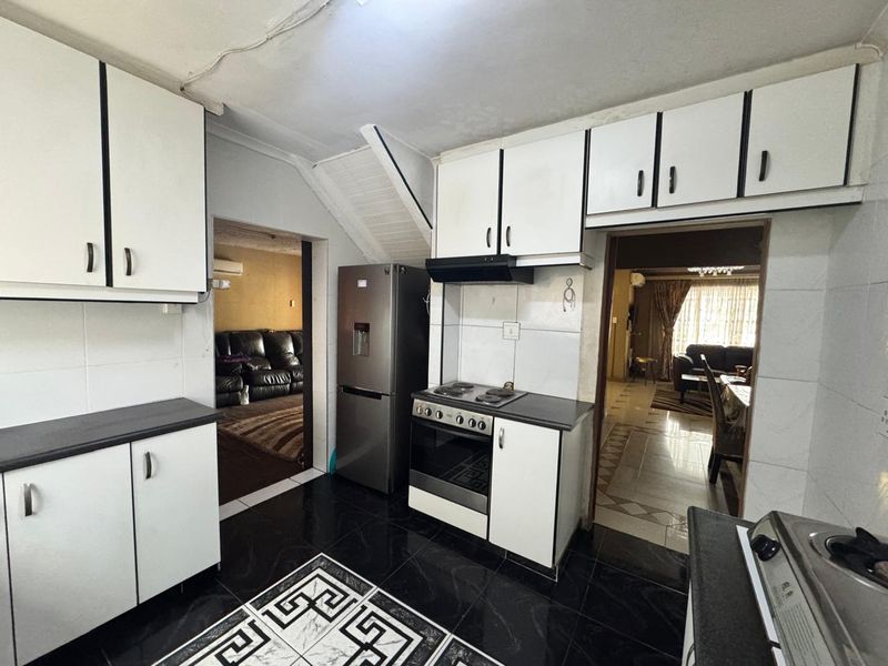 A functional kitchen featuring white built-in cabinetry, a dark countertop, an electric hob with extractor fan, and contrasting black and white tiled flooring.