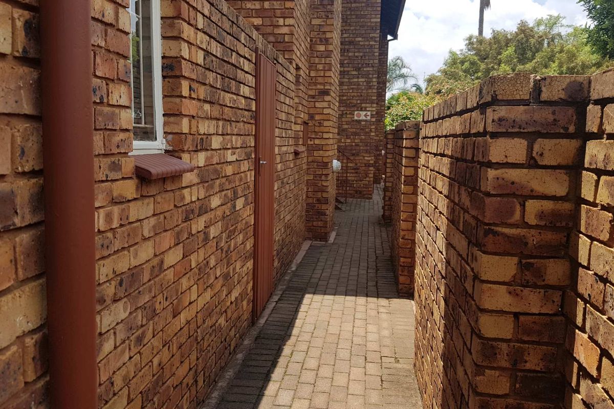 A narrow exterior walkway paved with concrete pavers, flanked by face-brick walls and featuring a side access door.