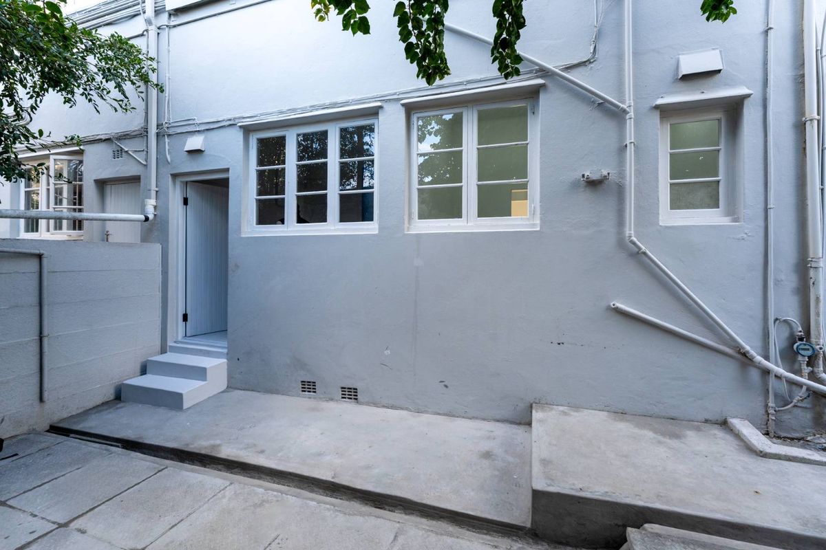 A rear exterior view of the apartment featuring a concrete patio area, painted masonry walls, and multiple window and door access points.