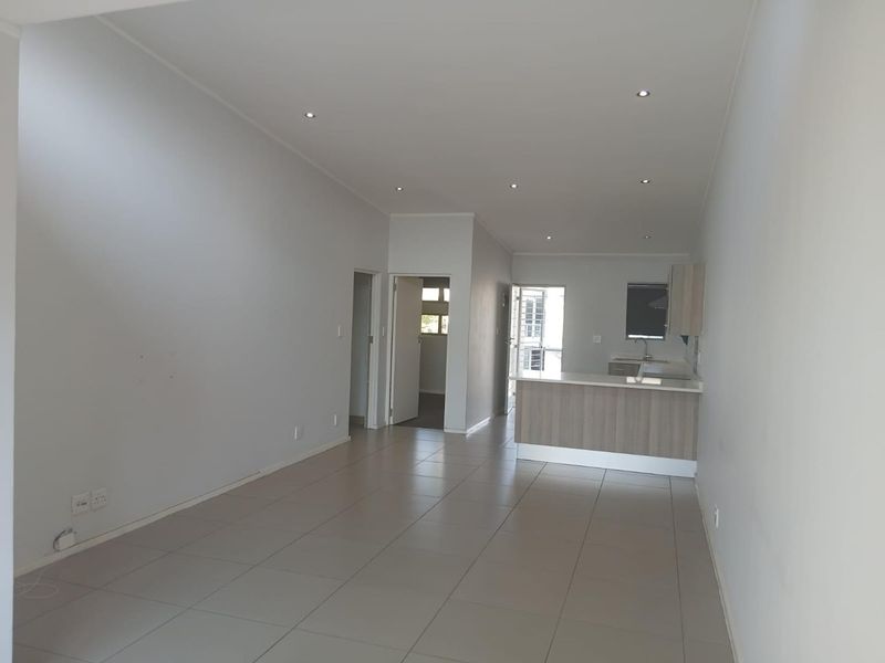 Spacious open-plan living area featuring neutral tiled flooring, recessed lighting, and a modern kitchen with a breakfast island.