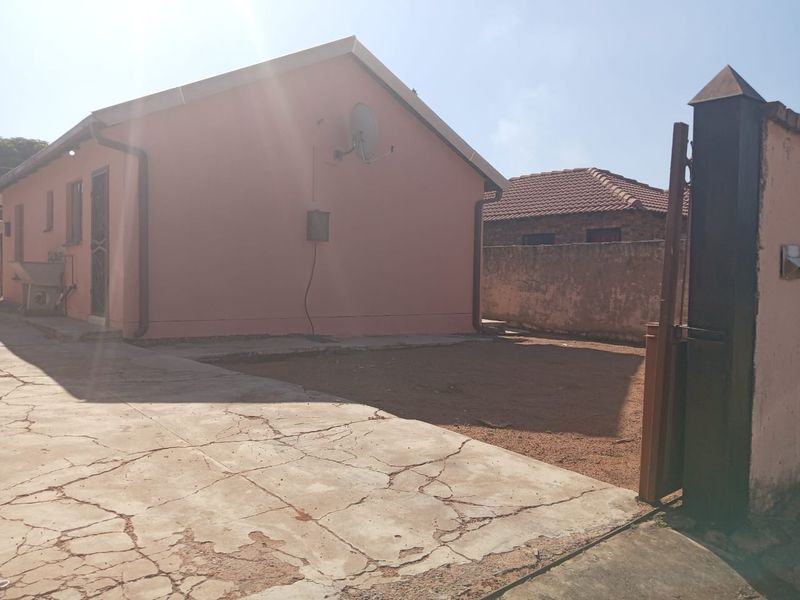 Front exterior view of the property featuring a concrete driveway, perimeter wall, and metal gate access.