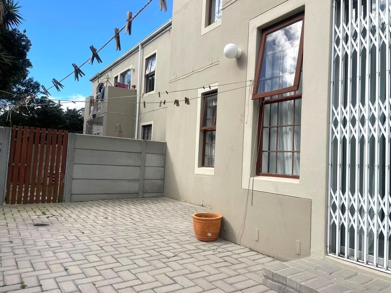 A paved rear courtyard area featuring a precast concrete boundary wall, timber gate, and secure access to the apartment interior.
