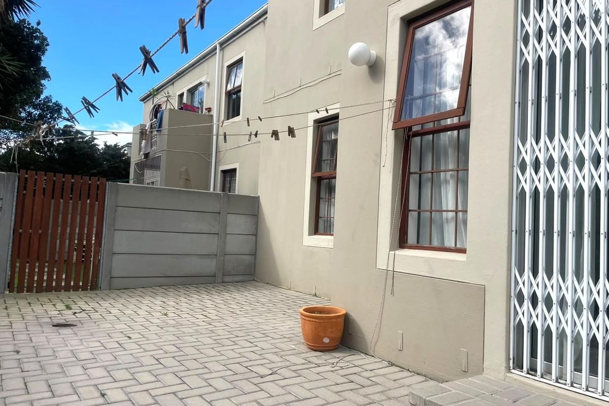 A paved rear courtyard area featuring a precast concrete boundary wall, timber gate, and secure access to the apartment interior.