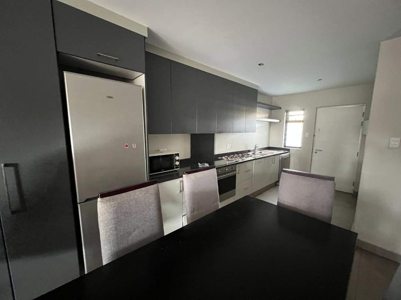 Modern kitchen featuring dark upper cabinetry, light lower cabinets, integrated oven, hob, and stainless steel sink, offering a functional and contemporary cooking space.