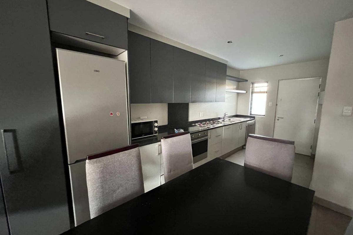 Modern kitchen featuring dark upper cabinetry, light lower cabinets, integrated oven, hob, and stainless steel sink, offering a functional and contemporary cooking space.