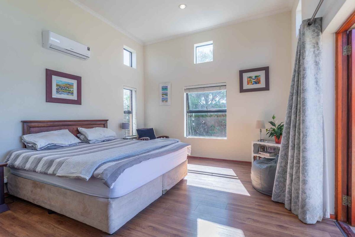Spacious bedroom featuring high ceilings, laminate flooring, split-system air conditioning, and direct access to an outdoor area through a wooden door.