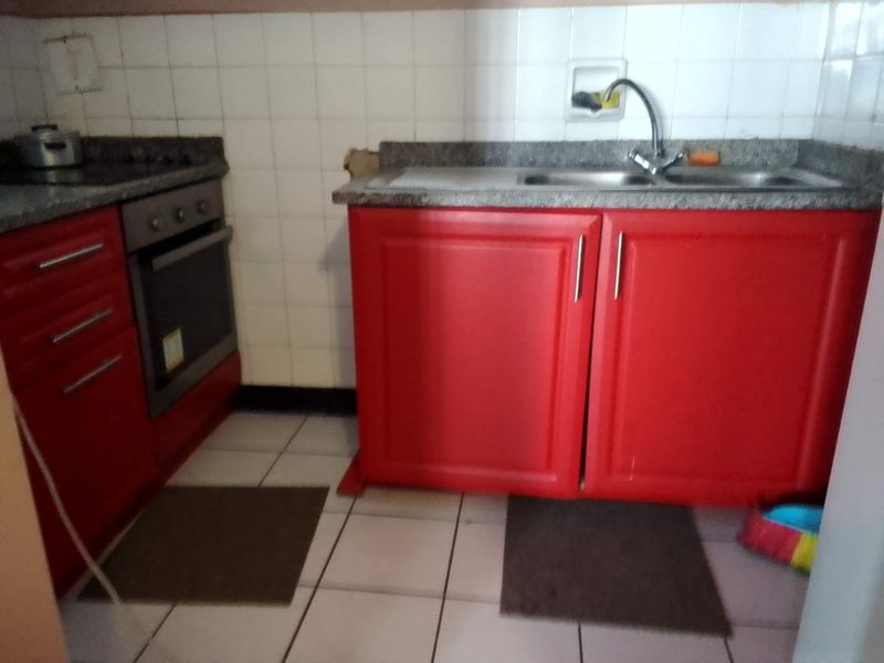 A compact kitchen featuring red cabinetry, granite countertops, a built-in oven, and a stainless steel sink with tiled backsplash.