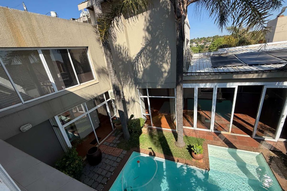 Rear courtyard area featuring a swimming pool with solar heating panels, tiled patio space, and large glass sliding doors providing access to the home.
