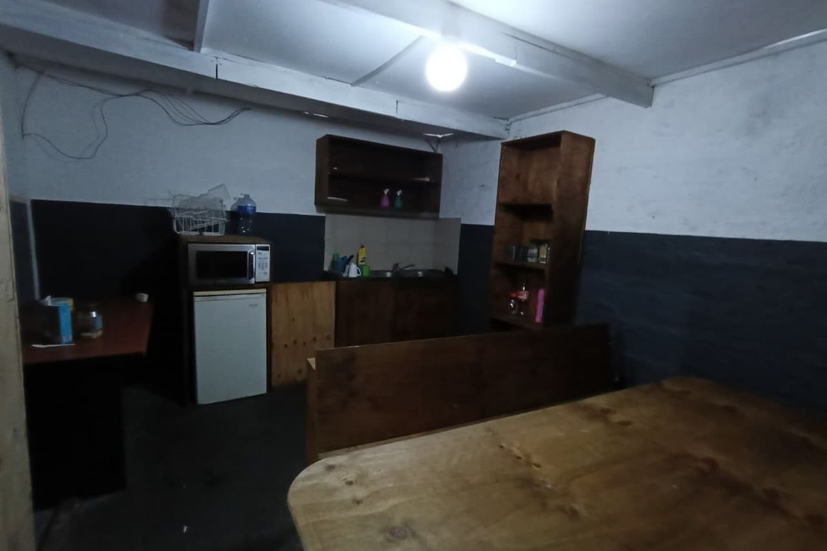 A basic kitchenette area featuring built-in wooden cabinetry, a sink, and exposed ceiling beams, requiring significant cosmetic updates and electrical finishing.