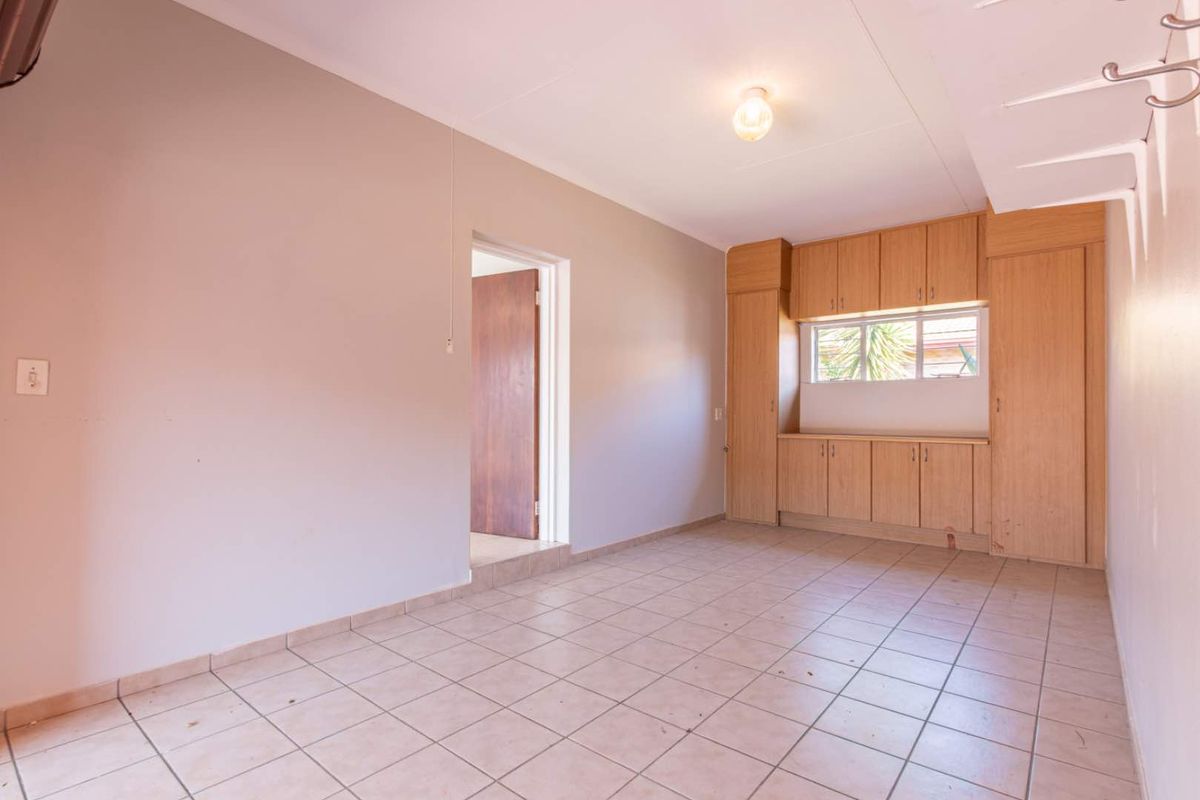 A functional bedroom or utility space featuring built-in wooden cabinetry, tiled flooring, and a window providing natural light.