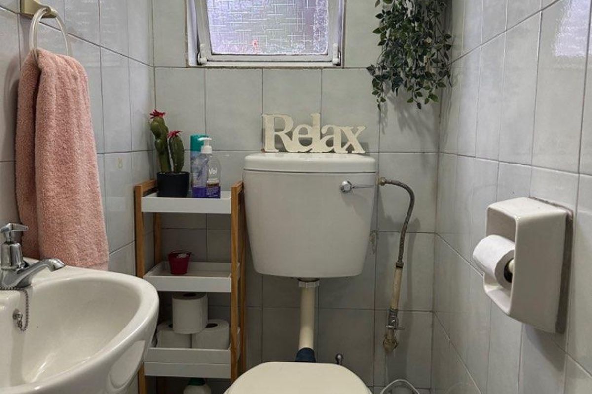 Compact bathroom featuring a pedestal basin, standard toilet, and tiled walls with a small frosted window for natural light.