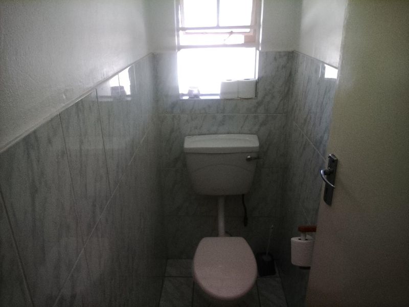 A compact, functional guest toilet featuring ceramic wall and floor tiling and a standard window for natural light.