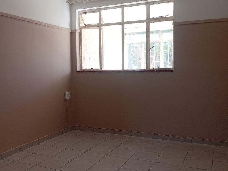 An empty bedroom featuring tiled flooring, a ceiling fan, and a large multi-pane window, offering a neutral canvas for personalization.
