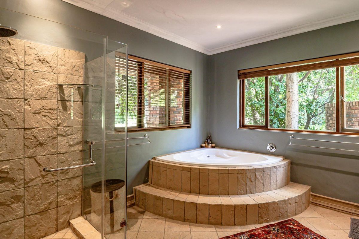 A well-appointed bathroom featuring a raised corner bathtub, a spacious walk-in shower with stone-tiled accents, and large windows providing natural light.