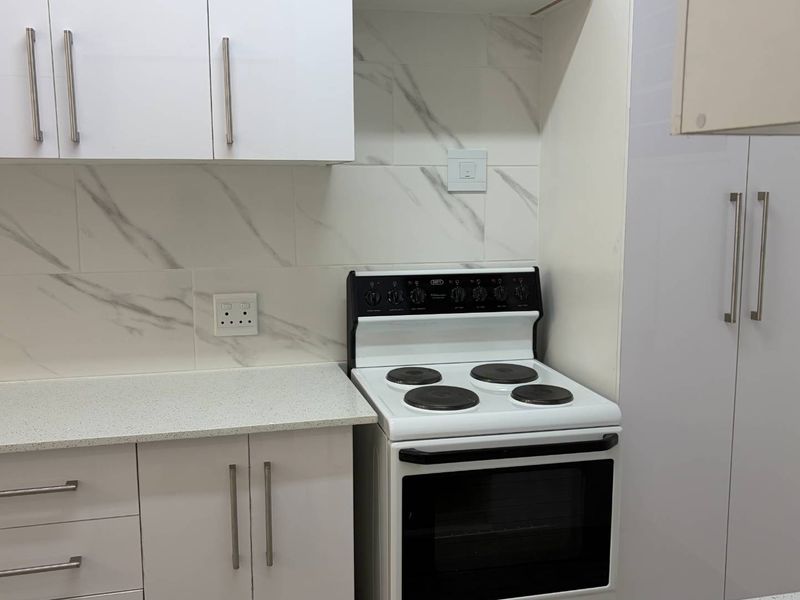 A modern kitchen featuring white cabinetry, marble-look tile backsplash, stone countertops, and a freestanding electric stove with oven.