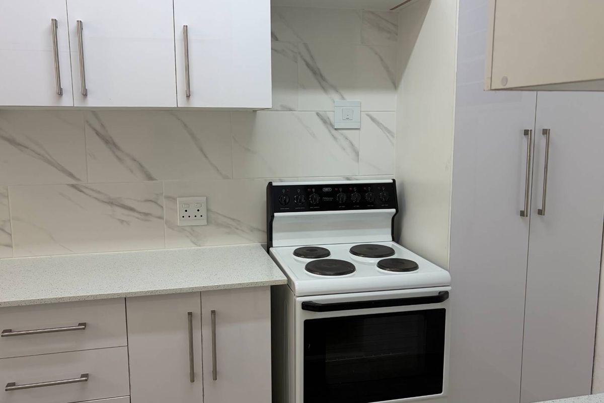A modern kitchen featuring white cabinetry, marble-look tile backsplash, stone countertops, and a freestanding electric stove with oven.