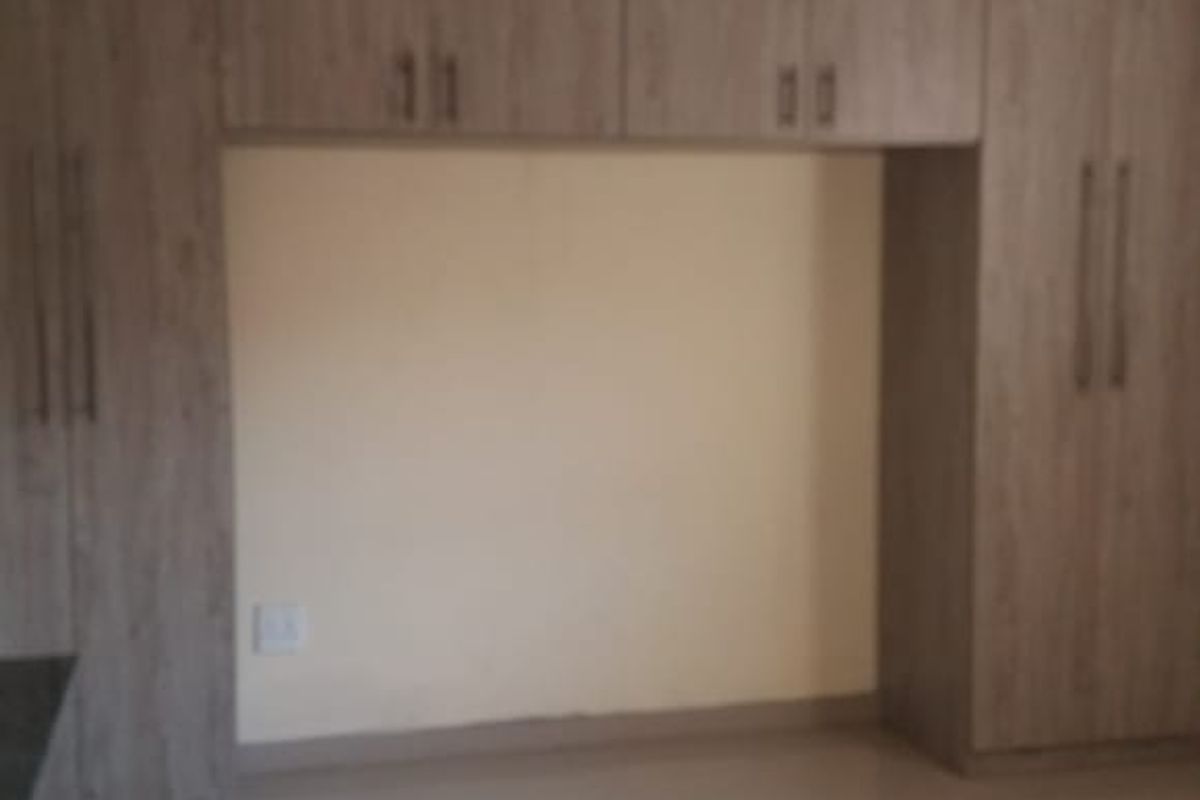 A clean, empty bedroom featuring modern wood-finish built-in cupboards and neutral tiled flooring.