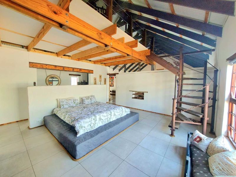Spacious bedroom featuring exposed timber beams, a mezzanine level, and a unique spiral staircase, set against a neutral tiled floor.