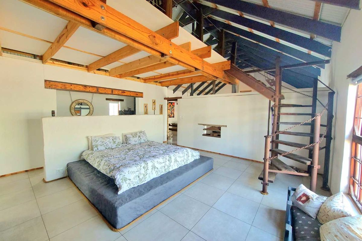 Spacious bedroom featuring exposed timber beams, a mezzanine level, and a unique spiral staircase, set against a neutral tiled floor.