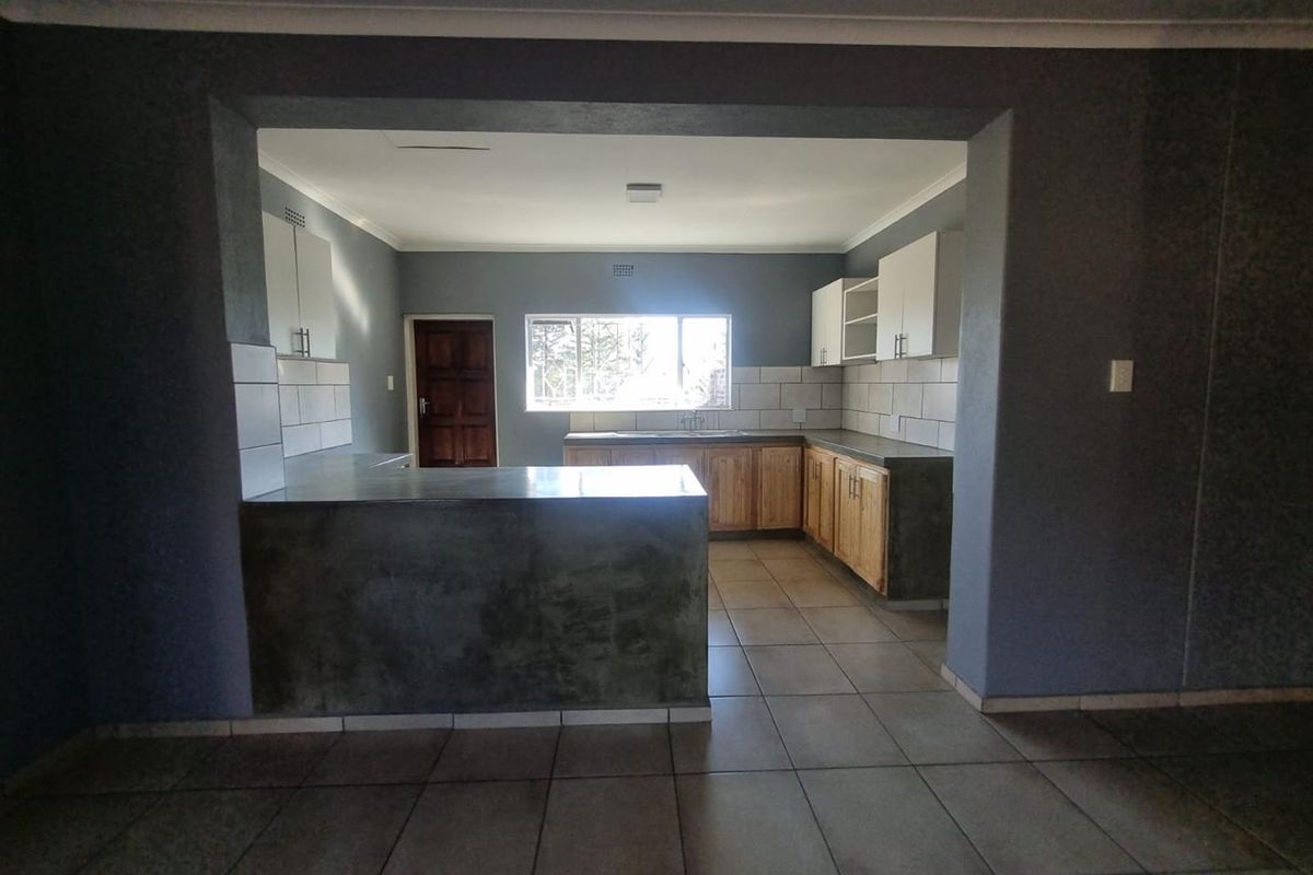 A spacious, empty kitchen featuring built-in timber cabinetry, concrete countertops, tiled backsplash, and tiled flooring, offering a functional layout ready for personalization.